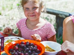 girl in red and white striped shirt holding white ceramic bowl with red and black fruits