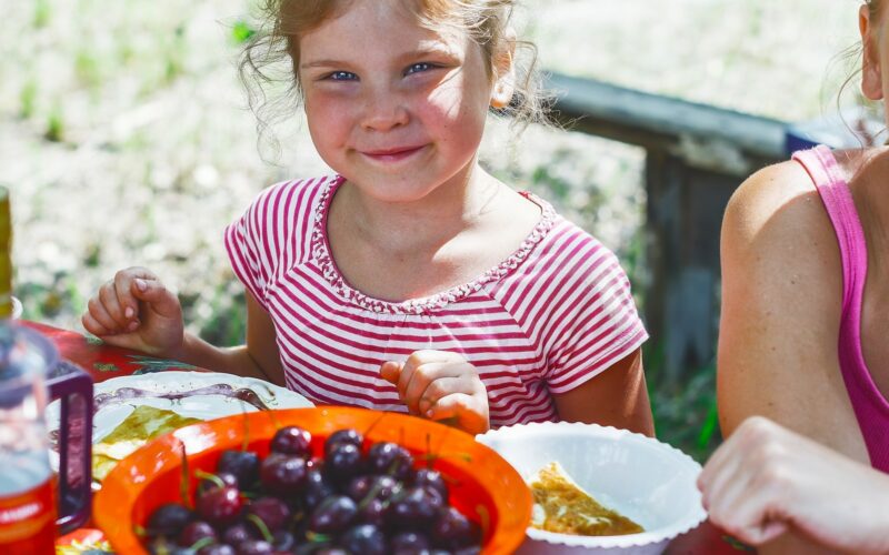 girl in red and white striped shirt holding white ceramic bowl with red and black fruits